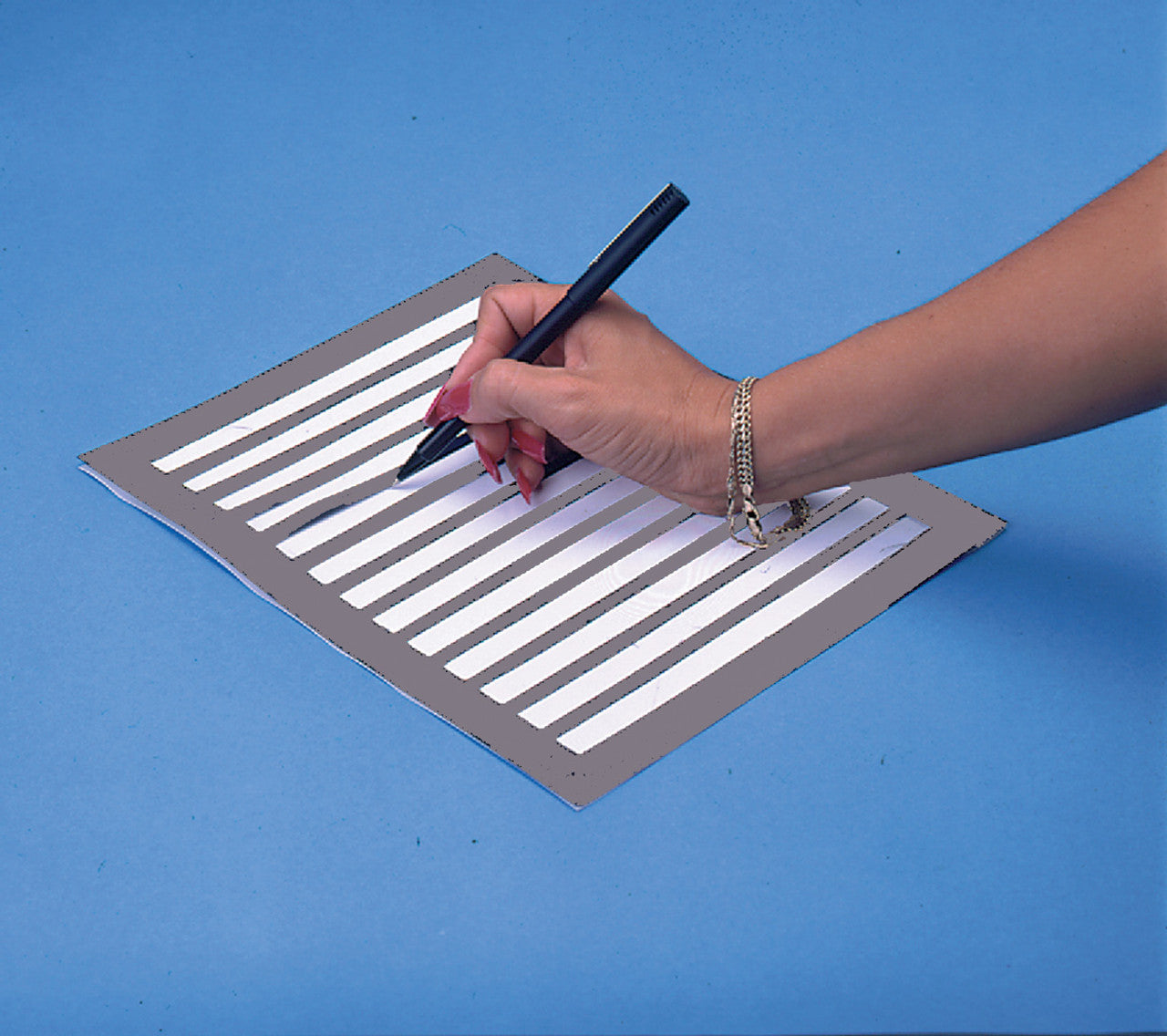 A person writing on a piece of paper that is lined with a black writing line guide.