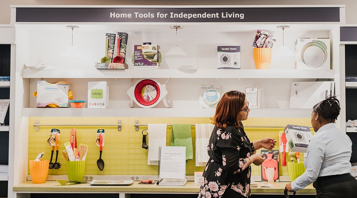 Two women standing at a wall of various products. The woman is holding a tactile timer box.