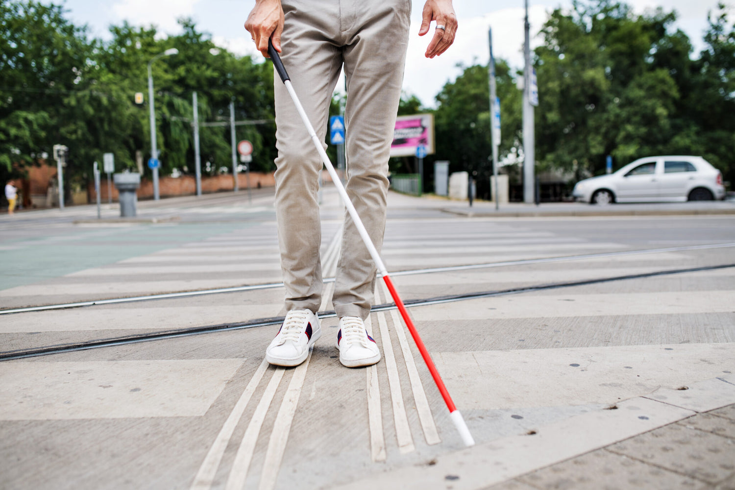 A man walking in an intersection using his white cane, with the image showing the man from the waist down.