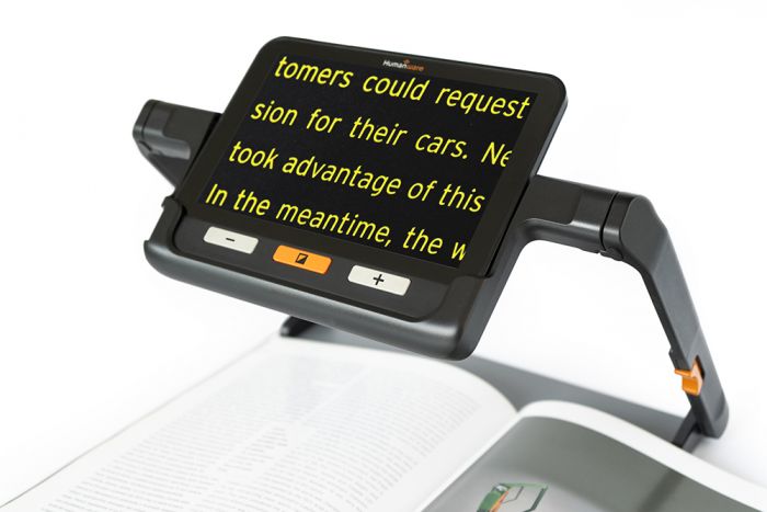 The Explore 8 Electronic Magnifier Device in its Foldable Stand, magnifying text on the tray below in yellow on black contrast.